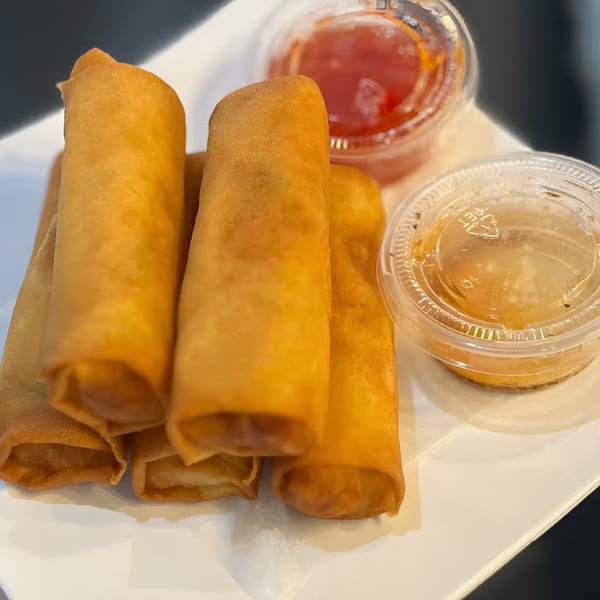 Golden-brown Filipino lumpia spring rolls with two dipping sauces on a white plate.