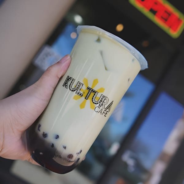 Hand holding a Kultura Cafe boba drink with a creamy top layer and dark pearls.