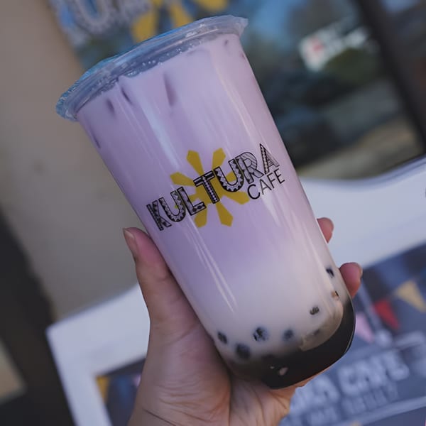 Hand holding a Kultura Cafe ube boba tea with a yellow sun logo.