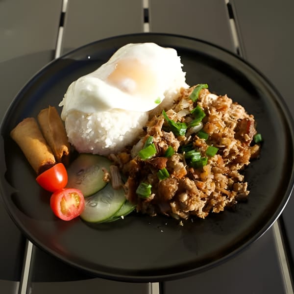Filipino sisig with rice, fried egg, spring rolls, cucumber, and tomatoes on a black plate.