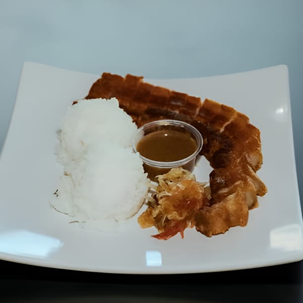Crispy pork belly, white rice, and a side of sauce and pickled vegetables on a white plate.