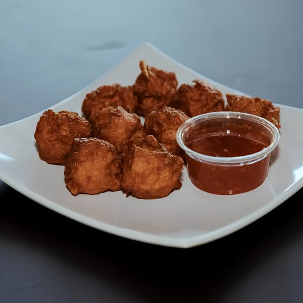 A white plate holds several golden-brown fried Filipino fritters next to a small cup of dipping sauce.