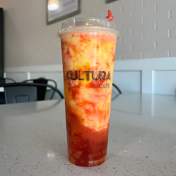 A Kultura Cafe mango and strawberry smoothie with a red straw stopper on a white speckled counter.