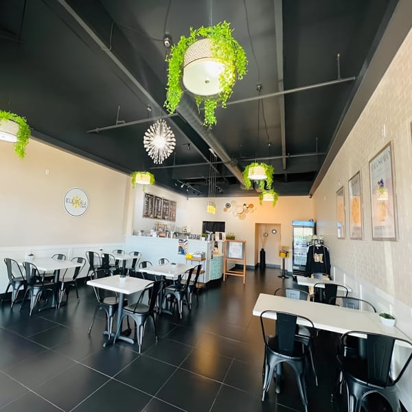 Interior of Kultura Cafe with black tables and chairs, white walls, and hanging green plants.