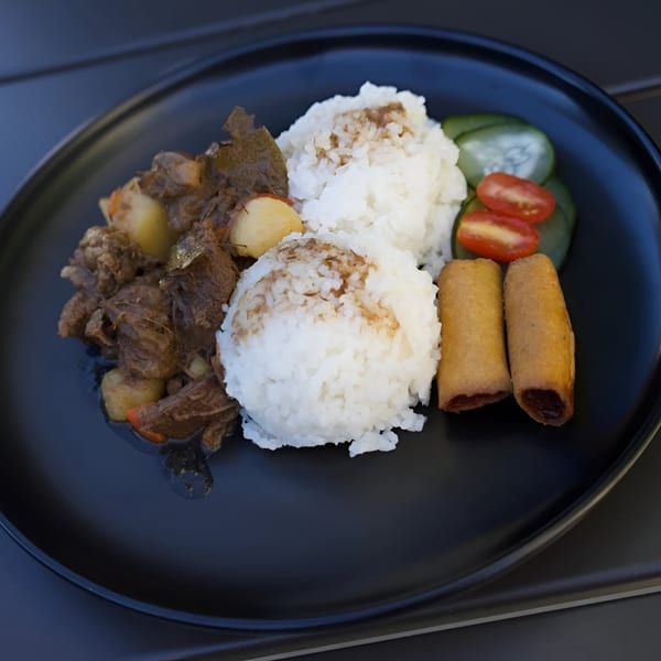 Filipino beef stew with potatoes, two scoops of rice, two lumpia, and sliced cucumbers and tomatoes.