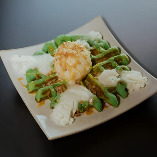 Green pandan waffles with vanilla ice cream, caramel drizzle, and whipped cream on a white plate.