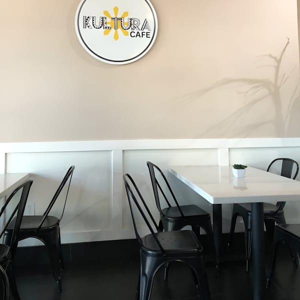 Interior of Kultura Cafe with a white logo, light walls, black chairs, and white tables.