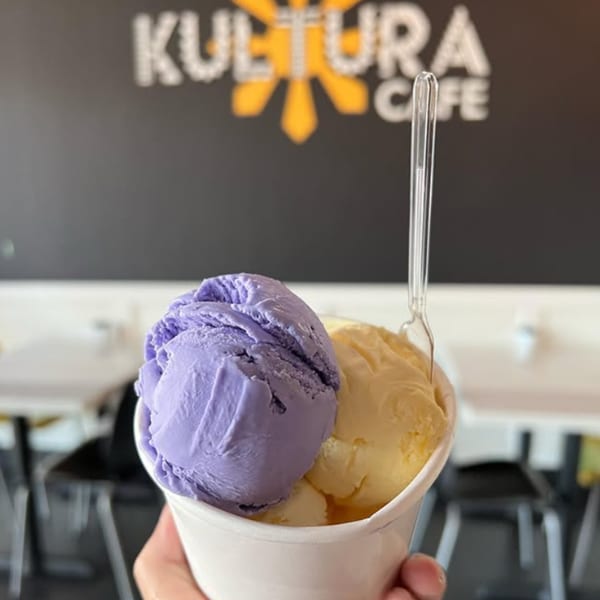 Hand holding a cup of purple ube and yellow mango ice cream with a spoon at Kultura Cafe.