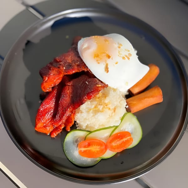 Filipino breakfast plate with red tocino, garlic rice, fried egg, hotdogs, and sliced vegetables.