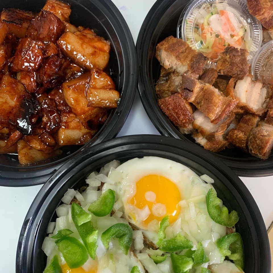 Three black bowls of Filipino food, including adobo, crispy pork belly, and a dish with fried eggs.